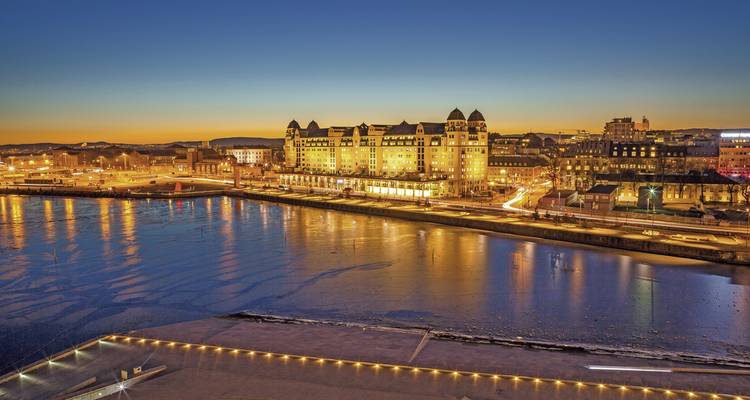 Stadtbild mit Lichtern, die sich bei Sonnenuntergang auf dem Wasser spiegeln.