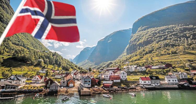 View of a village by a fjord with a Norwegian flag in the foreground.