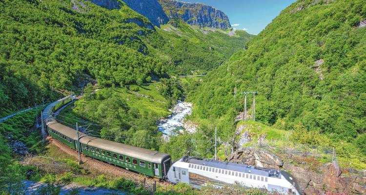 Train on a green mountainous route with a river below.
