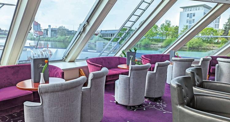 Salon sur un bateau de croisière avec des fauteuils violets et vue sur la rivière.