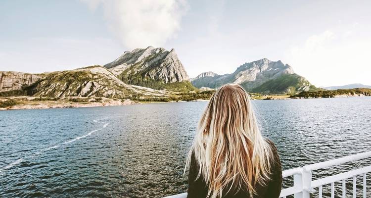 Eine Person, die von dem Deck eines Bootes aus eine Berglandschaft betrachtet.