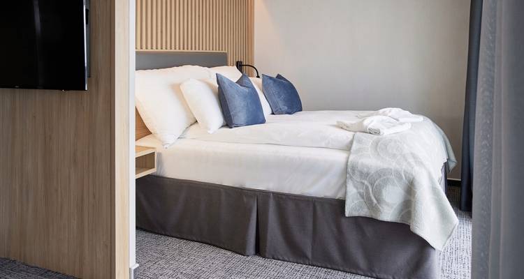 Ein gemütliches und modernes Hotelzimmer mit einem gemachten Bett mit Kissen und einer Decke.