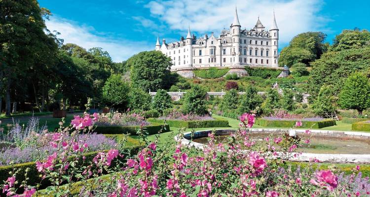 Großes Schloss mit makellosen Gärten und bunten Blumen im Vordergrund.