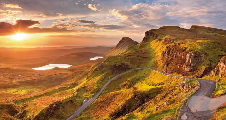 Malerische Bergstraße mit dramatischem Sonnenuntergangshimmel und sanften Hügeln.