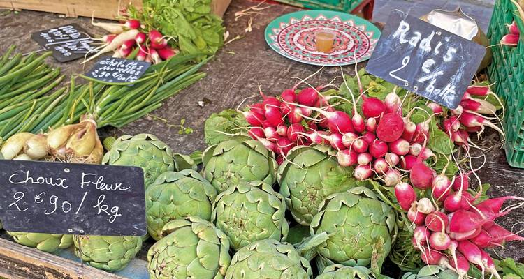 Fresh produce including radishes and artichokes on display, with price signs.