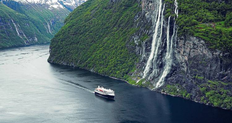 A cruise ship near a towering waterfall in a Norwegian fjord.