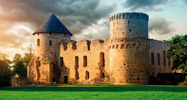 Un vieux château de pierre sous des nuages dramatiques dans un paysage herbeux.