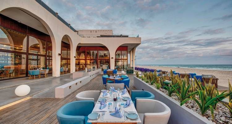 Buitenterras van restaurant met uitzicht op de oceaan en zonsondergang.