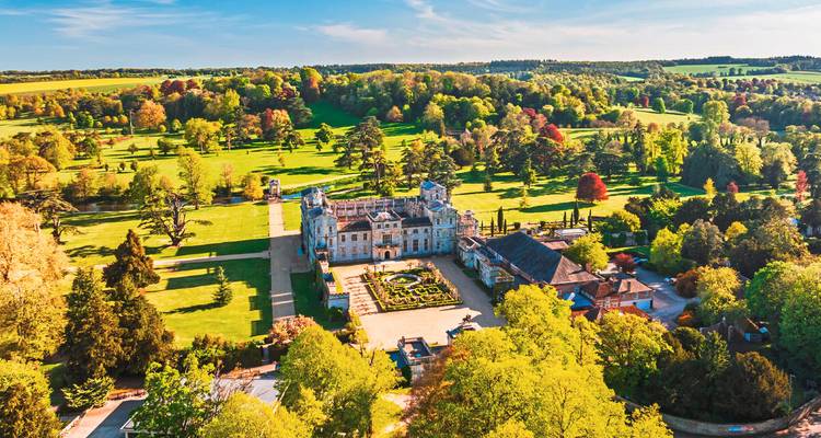 Groot landhuis omgeven door uitgestrekte groene gazons en kleurrijke bossen.