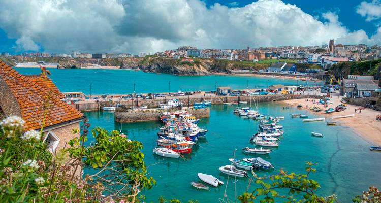 Los barcos de pesca llenan un brillante puerto cornualés de color turquesa con playas de arena y el pueblo más allá.