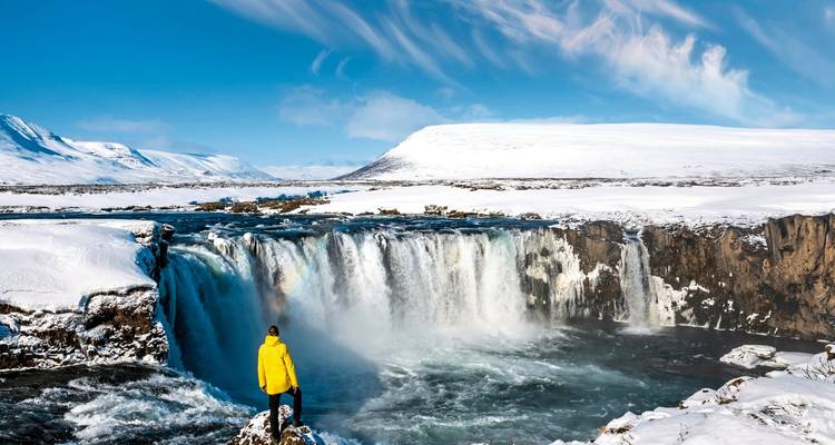 Cascade dans un paysage enneigé avec une personne en veste jaune.