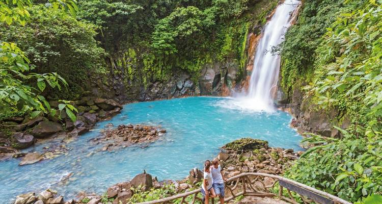Couple standing by a beautiful waterfall with bright blue waters.
