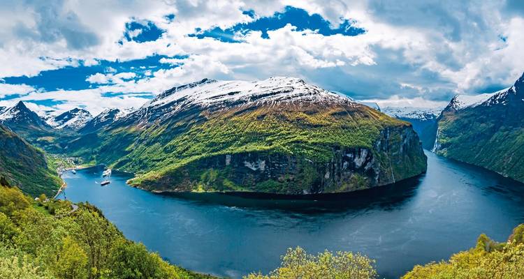Wide view of a fjord with snow-capped mountains and greenery.