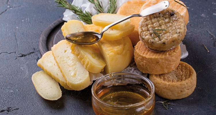 Eine Auswahl an Käsesorten begleitet von Honig, elegant präsentiert auf einer Schieferoberfläche.