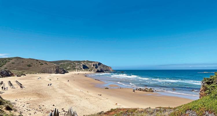 Plage de sable avec falaises et ciel bleu.