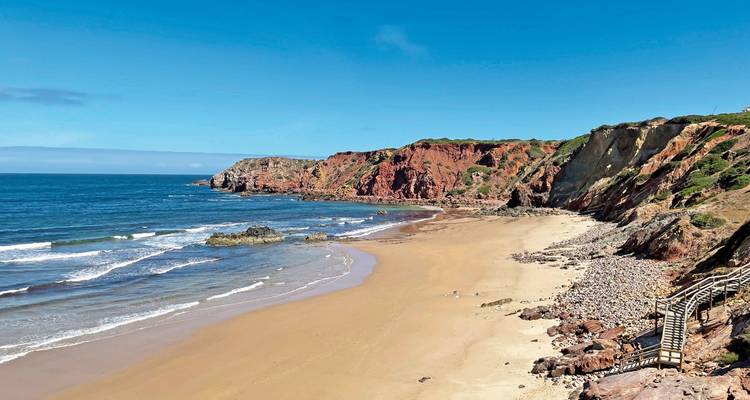 Plage avec falaises rouges et vagues de l'océan sous un ciel ensoleillé.