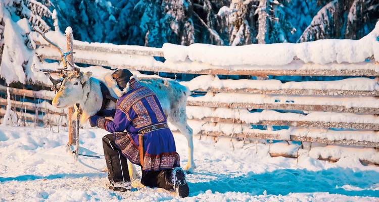 Personne en tenue traditionnelle avec un renne sur un fond enneigé.