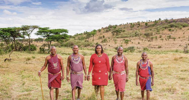 Gruppe von Menschen in traditioneller Maasai-Kleidung, die in der Savanne posieren.