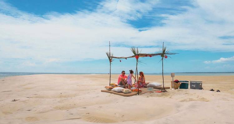 Paar genießt ein Picknick am Strand unter einem behelfsmäßigen Baldachin.