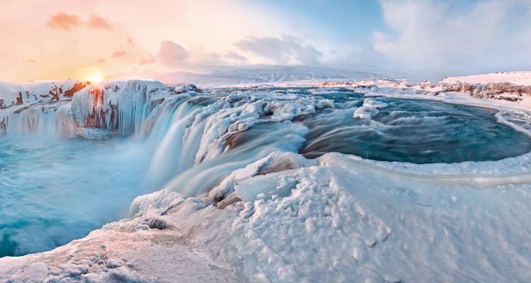 Frozen waterfall with icy surroundings and sunset lighting.
