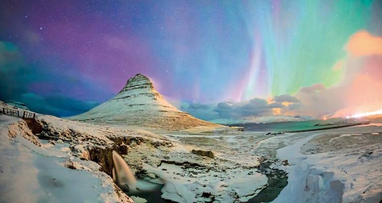 Northern lights over a snowy mountain and a small waterfall.