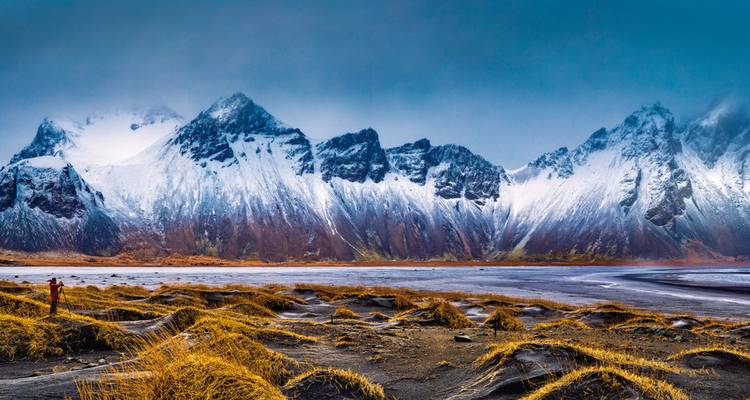 Snow-capped mountains with yellow grass and a person wearing a red jacket.