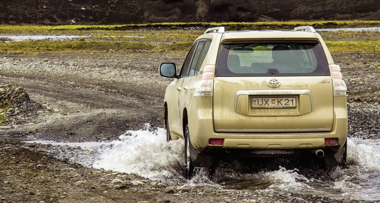 SUV überquert einen Wasserlauf in einer zerklüfteten Landschaft.