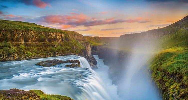 A powerful waterfall with mist and a colorful sky.