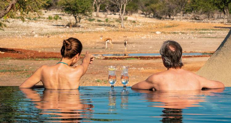 Couple relaxing in a pool with a view of wildlife in the distance.