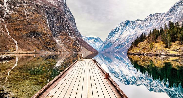 Wooden pier extending into a fjord surrounded by rocky mountains.