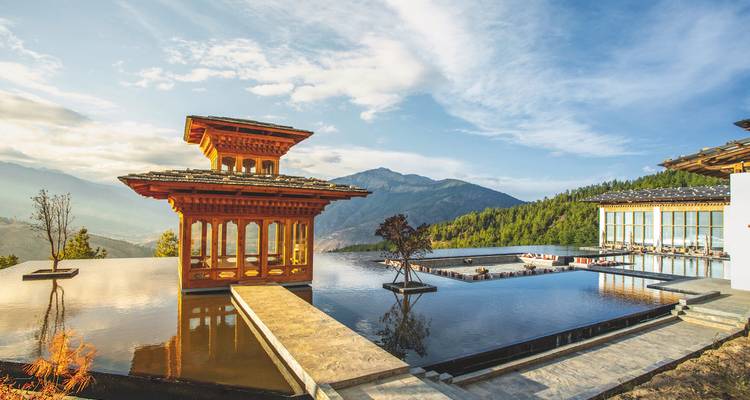 Traditionelle bhutanische Architektur mit Reflexionsteichen vor einer Bergkulisse.