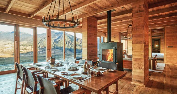 Rustikales Esszimmer mit warmem Kaminblick und Bergen in der Ferne.
