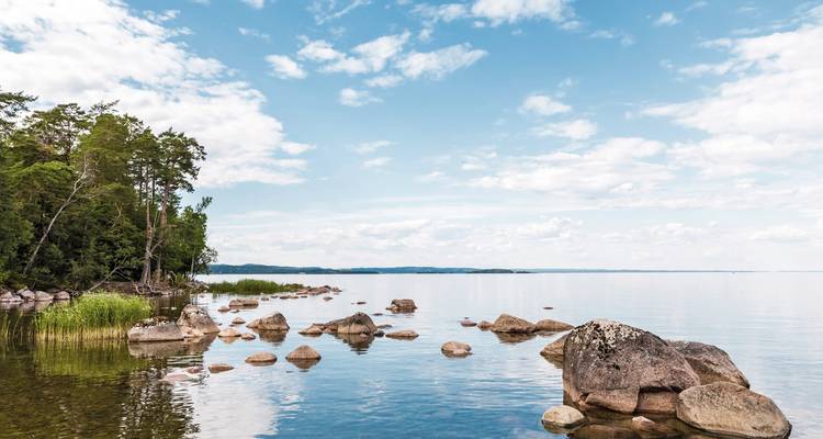 Lac calme avec des rochers et un ciel dégagé, entouré de verdure.