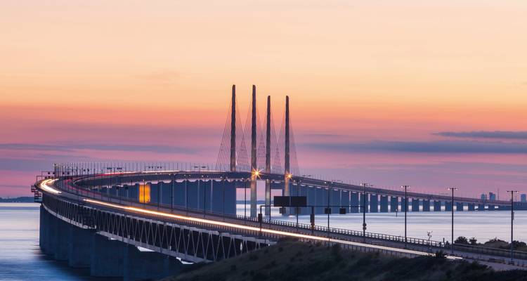Eine lange Brücke über dem Meer bei Sonnenuntergang mit Lichtspuren.