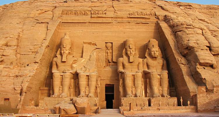 Grand statues of pharaohs carved into a rocky cliff.