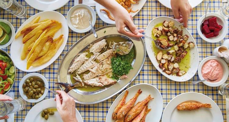 Gemengde mediterrane gerechten op een tafel met handen die naar de schalen reiken.