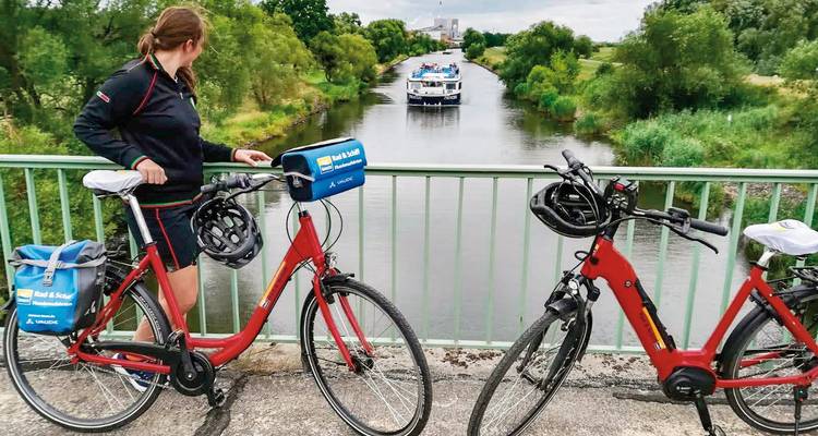Mensen op fietsen die een gracht bekijken met een voorbijvarende boot.