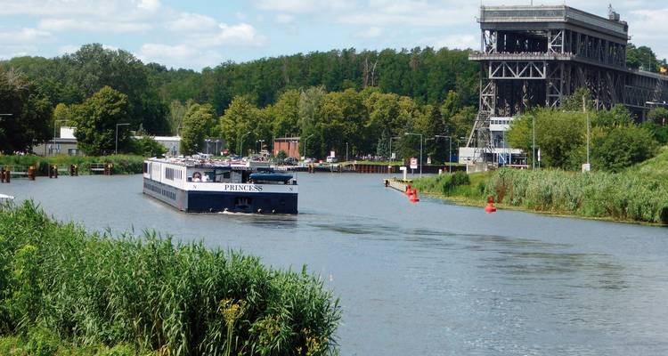 Een riviergezicht met een cruiseschip genaamd 'Princess' dat vaart, en een constructie die lijkt op een scheepslift of industrieel gebouw.