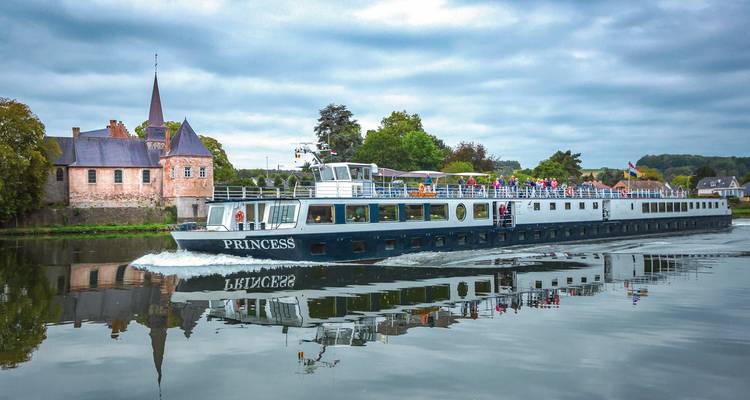 Het cruiseschip 'Princess' dat langs een kasteelachtig gebouw en reflecterend wateroppervlak vaart.