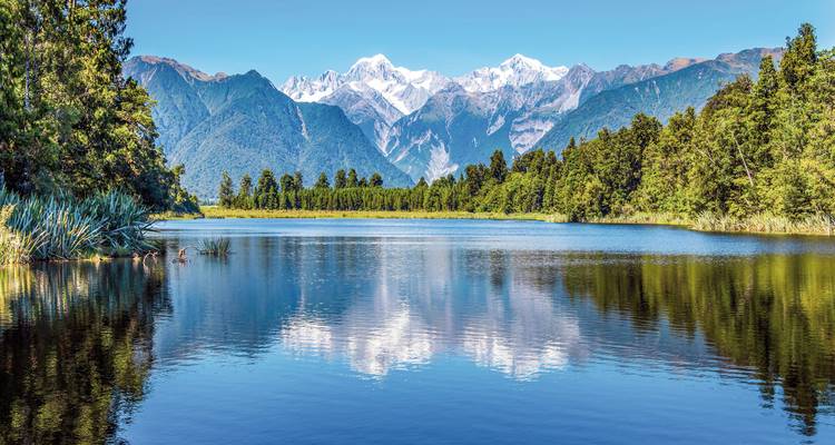 Schneebedeckte Berge spiegeln sich in einem ruhigen See.