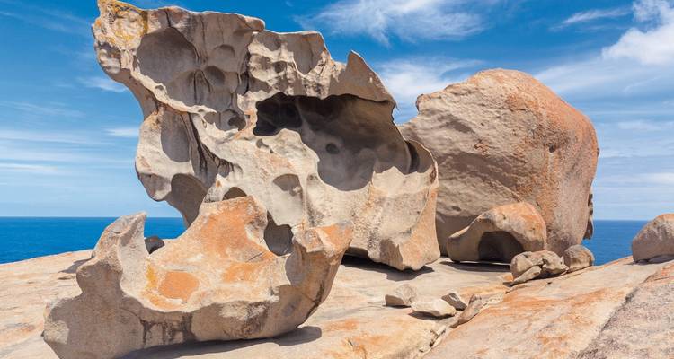 Des rochers de granit aux formes spectaculaires, sculptés par le vent et perchés sur une falaise côtière avec l'océan bleu en arrière-plan.