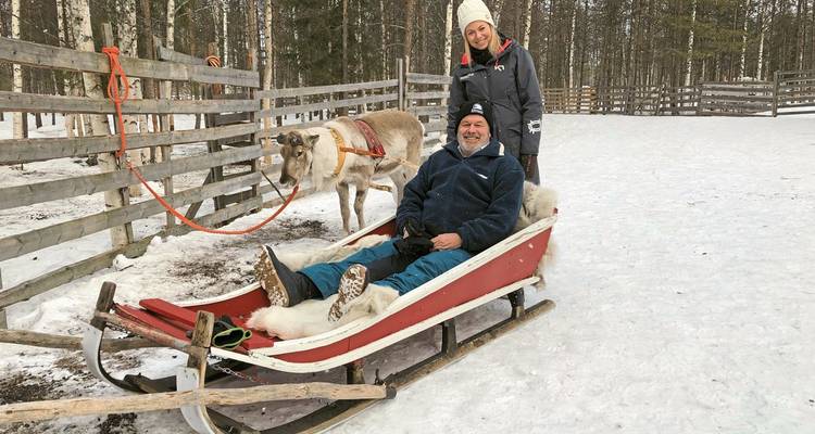 Deux personnes sur un traîneau avec un renne dans une zone clôturée enneigée.