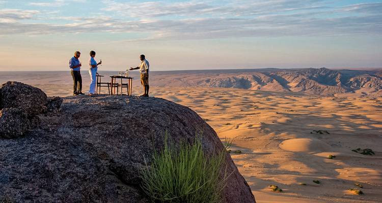 Menschen, die auf einem Felsen speisen und auf Wüstendünen blicken.