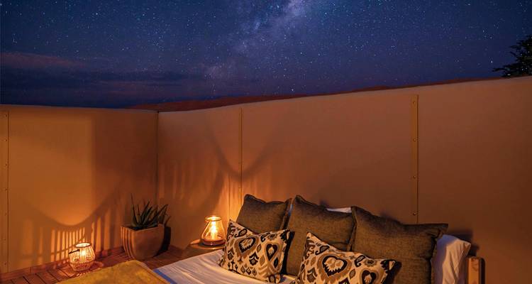 Außenbereich mit einem Bett unter einem sternenklaren Nachthimmel.