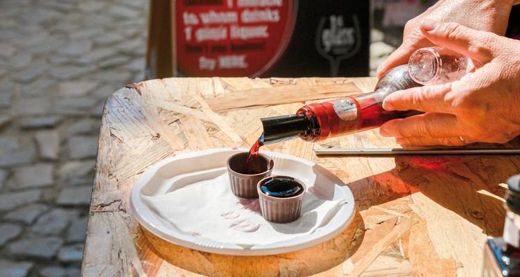 Hände, die Wein in Becher an einem Straßenmarkt eingießen.