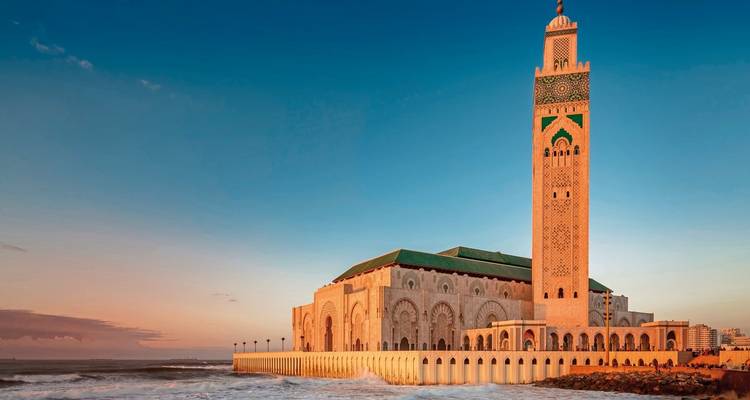 Una gran mezquita con un minarete junto al mar durante el atardecer.