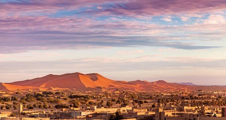 Ein Blick über eine Stadt vor der Kulisse sanft geschwungener orangefarbener Sanddünen.