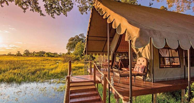 Tente de safari de luxe surplombant un delta au coucher du soleil.