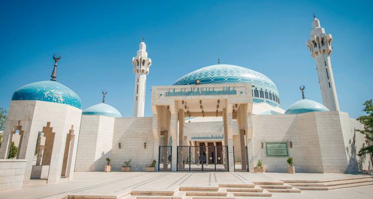 Weiße Moschee mit blauen Kuppeln unter klarem blauen Himmel.