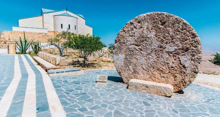 Runde Steinstruktur mit historischer Stätte im Hintergrund.